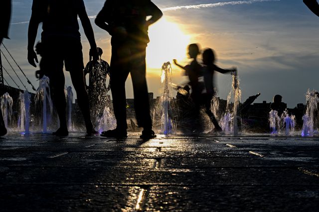 Children cool off by playing in a fountain in Domino Park, Brooklyn with the Manhattan skyline in the background as the sun sets during a heat wave on July 24th, 2022.
